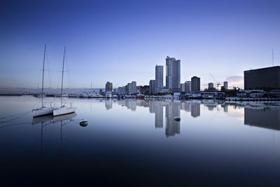 Sailboats in city by buildings against clear sky