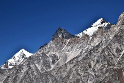 Low angle view of snowcapped mountains against clear blue sky