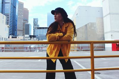 Young woman looking away while standing by railing in city