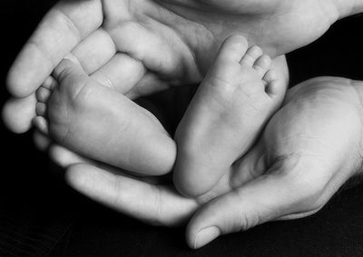 Cropped image of mother holding legs of baby over black background