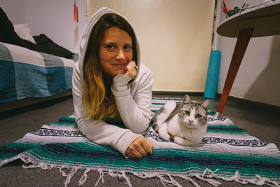 Portrait of smiling woman with cat sitting on floor at home