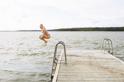 Full length side view of excited woman jumping into lake