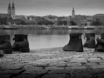 Close-up of shoes by river in city against sky