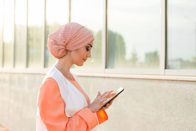 Midsection of woman holding mobile phone while standing on window