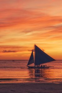 Sailboat sailing on sea against orange sky