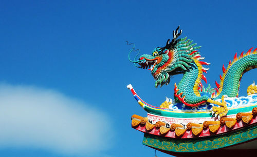 Low angle view of dragon sculpture at temple against blue sky