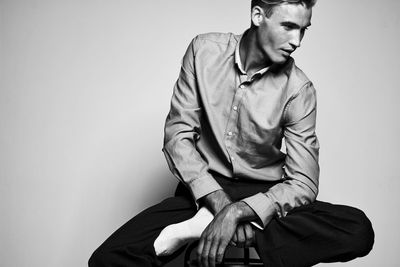 Young man looking away while sitting against wall