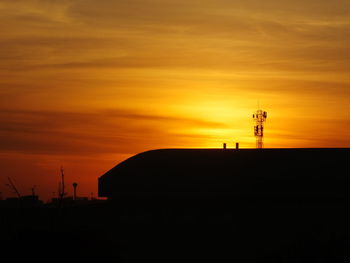 Silhouette tower by building against orange sky