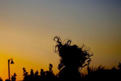 Cropped image of silhouette girl with tousled hair against sky during sunrise