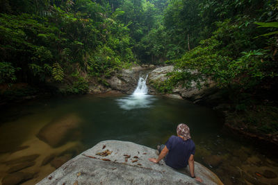 Person sitting on rock looking at stream flowing through rocks in forest