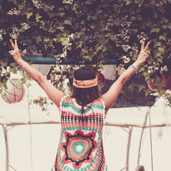 Rear view of woman gesturing peace sign against tree