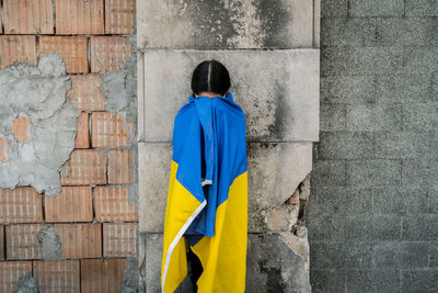 Girl wrapped in ukrainian flag against wall