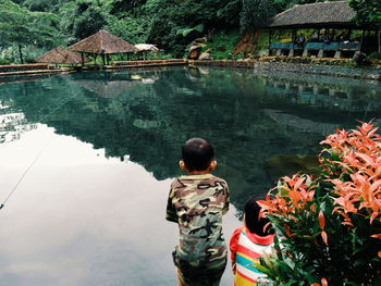 Rear view of boy looking at lake against building