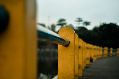 Close-up of yellow railing by street against sky