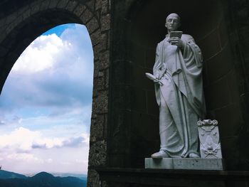 Low angle view of statue by archway against sky