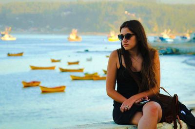 Beautiful woman sitting on retaining wall against sea