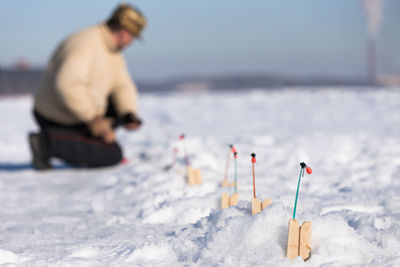 Focus on fishing nets for ice fishing, blurred fisherman checks fishing rod, sunny winter frosty day