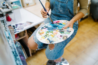 Crop anonymous artist taking paint from colorful art palette while creating artwork in art studio