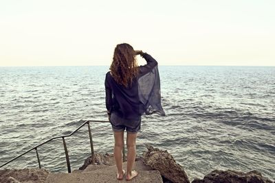 Rear view of woman standing on steps by sea