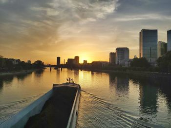 Scenic view of river by buildings against sky during sunset