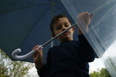 Low angle view of boy holding umbrella while standing outdoors