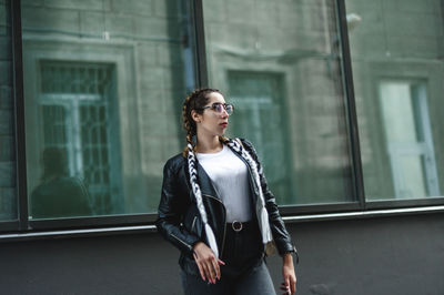 Beautiful young woman looking away standing against building in city