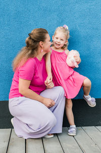 Portrait of smiling mother and daughter sitting on footpath