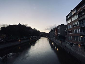 Canal amidst buildings in city against sky during sunset