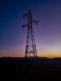 Low angle view of silhouette electricity pylon on field against sky at sunset