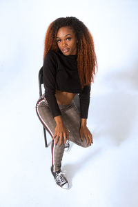 Portrait of young female model sitting on chair against white background