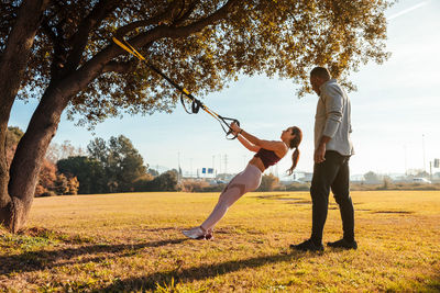 Full length of man assisting friend in exercising at public park