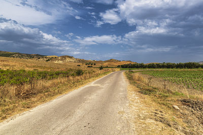 Empty road amidst field against sky