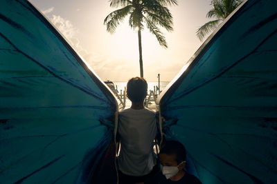 Rear view of woman and boy standing by palm trees against sky