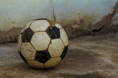 Close-up of abandoned soccer ball on footpath against wall