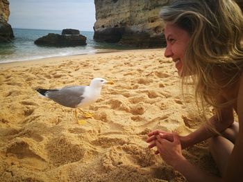 Side view of young woman with seagull on beach