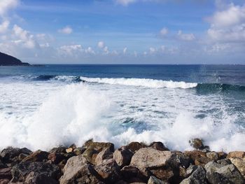 Waves splashing on rocks at shore against sky