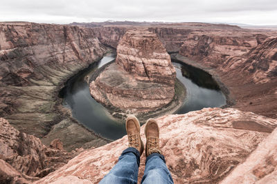 Low section of man on rock formation against sky