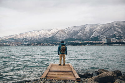 Rear view of man looking at lake against mountain range