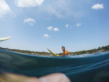 Water surface shot of shirtless man surfing in sea against sky