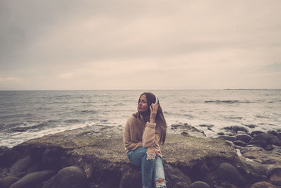 Woman sitting on rock at beach against sky