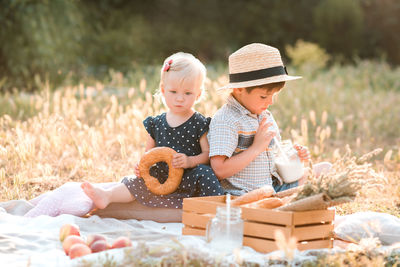 Cute brother and sister sitting on picnic blanket in park