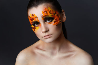 Close-up portrait of young woman with make-up against gray background