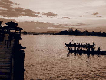Silhouette people on pier at lake against sky during sunset