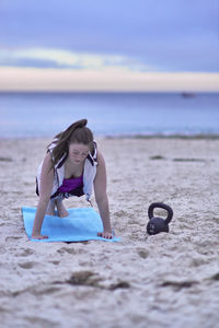 Woman exercising at beach against cloudy sky