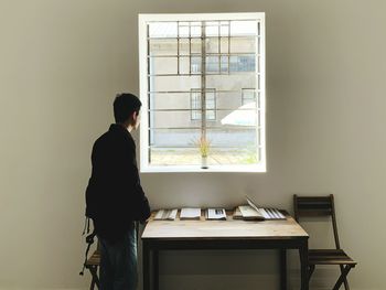 Rear view of man standing by window at home