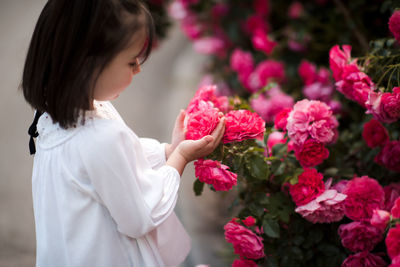 Cute little baby girl 3-4 year old holding pink roses in garden closeup. summer season. childhood.
