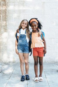 Laughing african american girl embracing friend standing on street in bright day