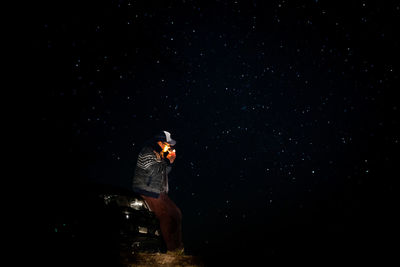 Man smoking cigarette while standing on field at night