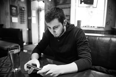 Young man using mobile phone by beer glass on restaurant table