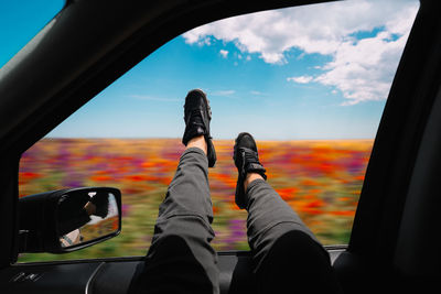 Low section of peopleon traveling on car against colorful meadow and sky in summer